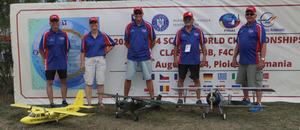 Team posing with model airplanes in front of a championship banner.
