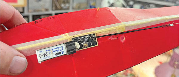 Red model aircraft wing with electronic components attached.