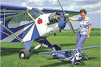 Woman standing next to a large blue and white plane and a small model plane on grass.