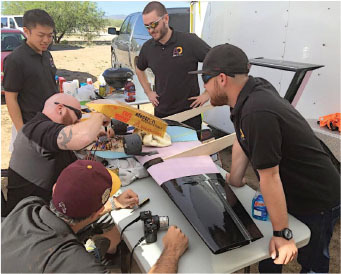 Group of people working on a drone at a table outdoors.