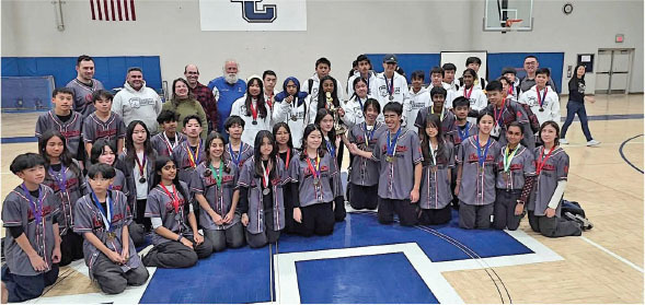 Group photo of students and adults in a gym, some holding trophies, wearing medals.
