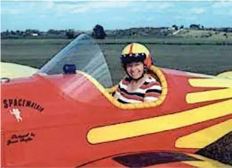 Smiling person in a striped shirt sits in a red and yellow plane labeled "Spacewalker."