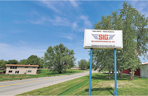 SIG Manufacturing Co. Inc. sign by a road, trees, and buildings in a rural setting.