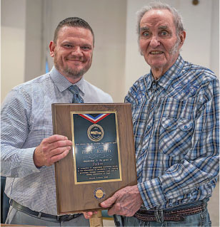 Two men smiling, holding an award plaque.