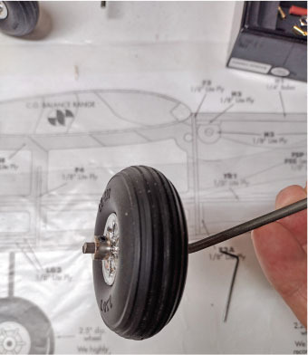 Hand holding a model airplane wheel against a blueprint background.