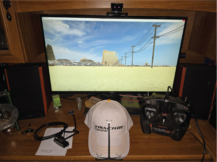 Computer setup with desert landscape on screen, TrackIR hat, and remote control on desk.