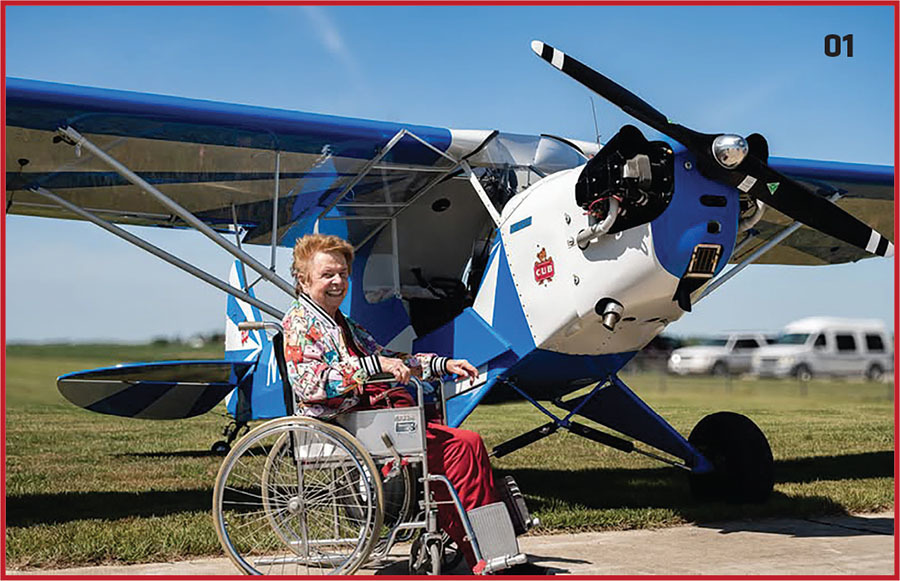 A person in a wheelchair smiling beside a small blue and white airplane.