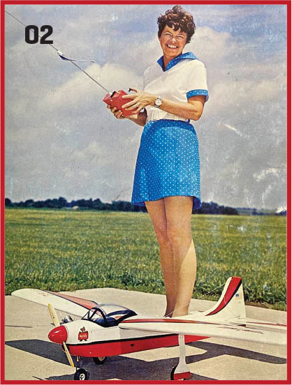 Woman in blue dress holding radio control near model airplane on runway.