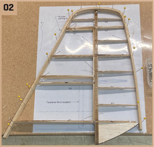 Wooden airplane tail section assembly on blueprint with yellow pins.