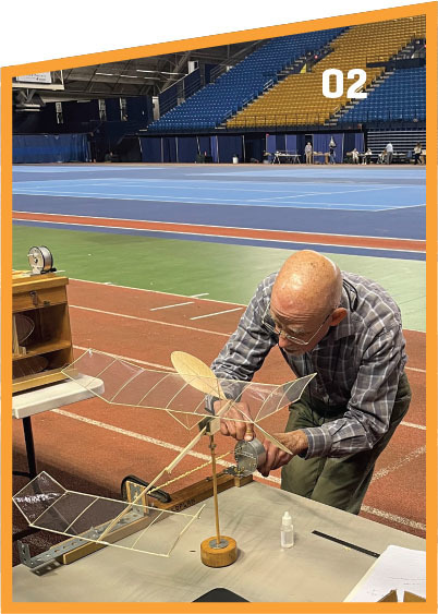 Man adjusting a model airplane in a sports arena.
