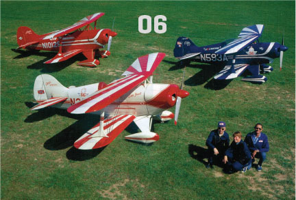 Four colorful model planes on grass with three people sitting nearby; number "06" above.