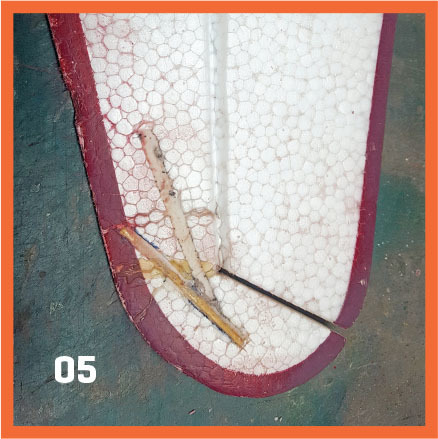 Broken model plane wing with red border on green surface, labeled "05".