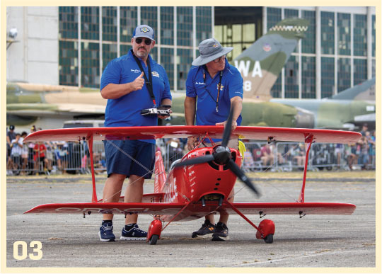 Two men stand beside a small red aircraft on the tarmac.