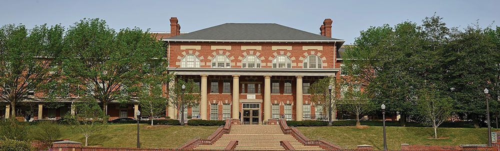 Red-brick building with columns, surrounded by trees, under a clear sky.
