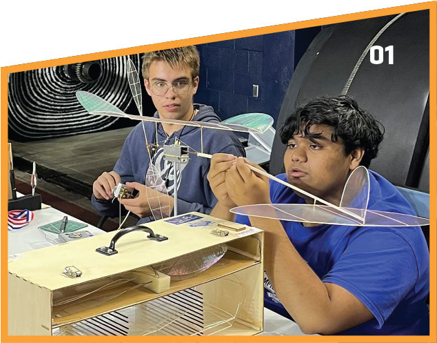 Two students assemble a model aircraft indoors, focused and engaged.