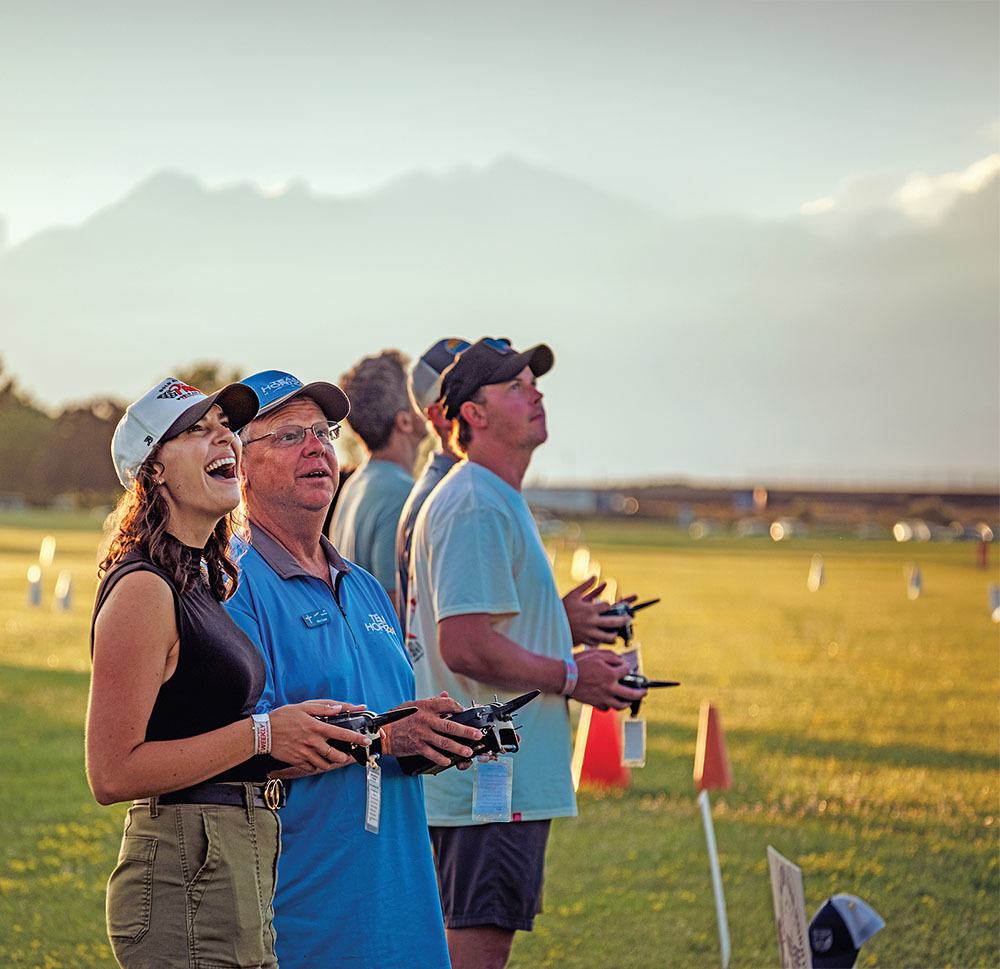 People flying drones in a sunny field, smiling and focused.