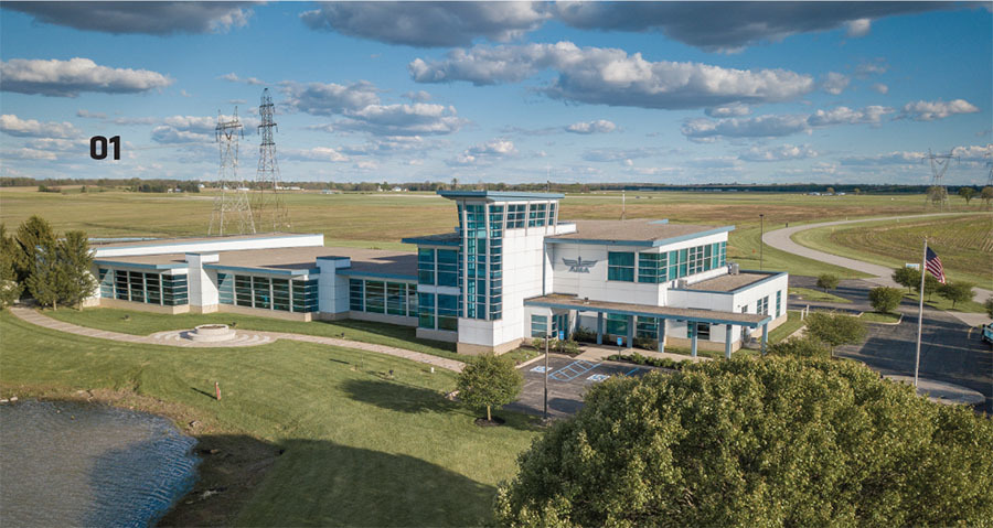 Modern building surrounded by greenery, under a partly cloudy blue sky.