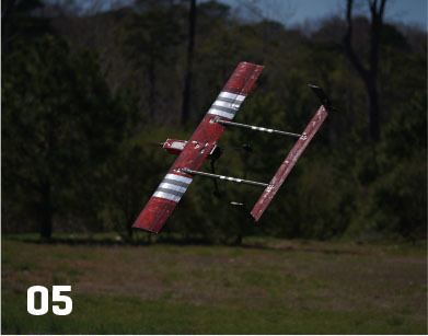 Red model airplane flying above grassy field, labeled "05".