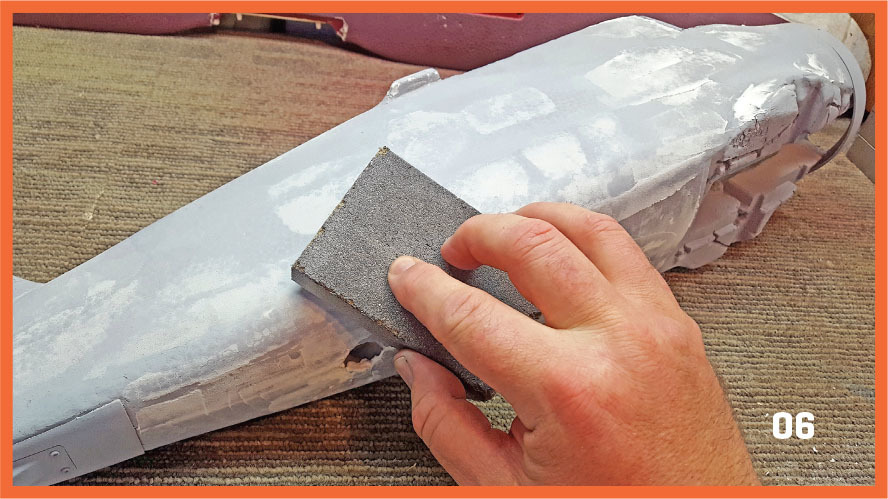 Hand sanding foam model airplane, number "06" in the corner.