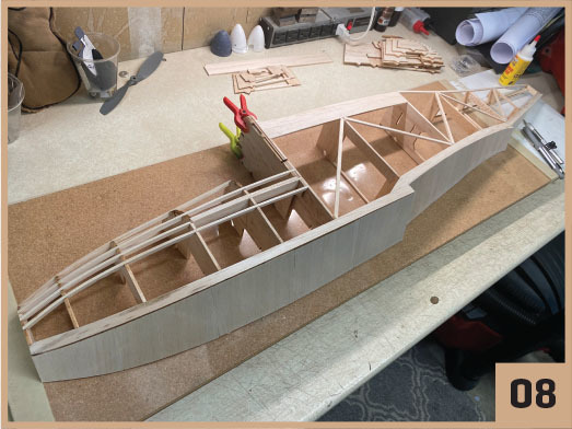 Model ship frame on a workbench, labeled "08" in the corner.