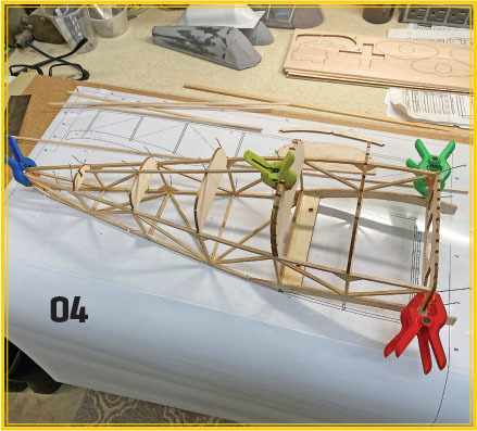 Wooden model airplane frame with clamps on a workbench.