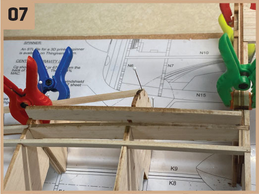 Wooden model airplane under construction with colorful clamps.