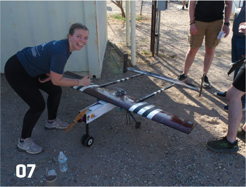 Woman squatting by a model aircraft, smiling. Number "07" at the bottom left.