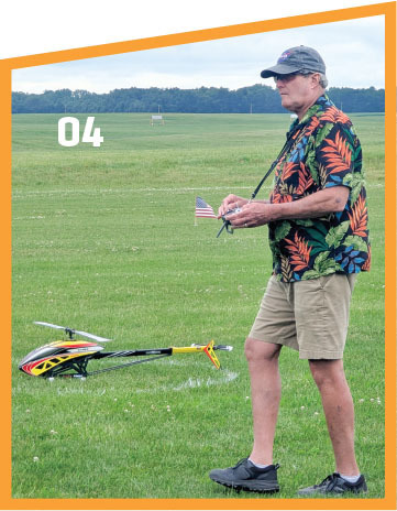 Man flying model helicopter in grassy field, number 04 visible.