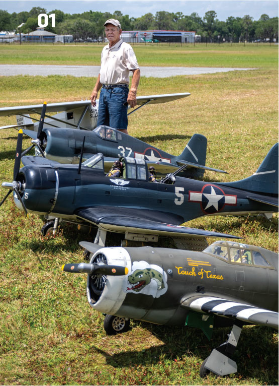 Man standing on grass with large model airplanes.