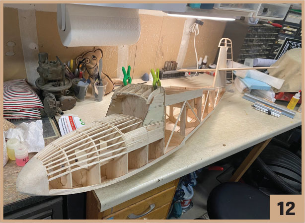 Wooden model airplane under construction on a cluttered workbench.