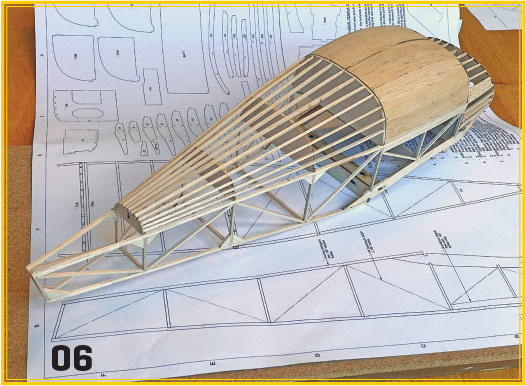 Wooden model airplane fuselage on blueprint. Number "06" visible.