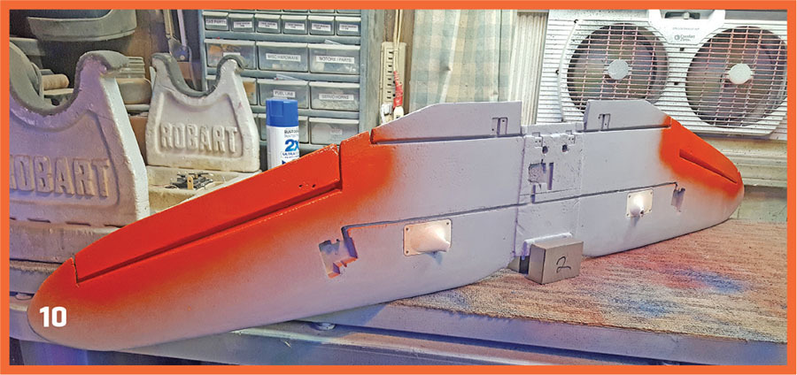 Airplane wing with red and gray paint on a workbench.