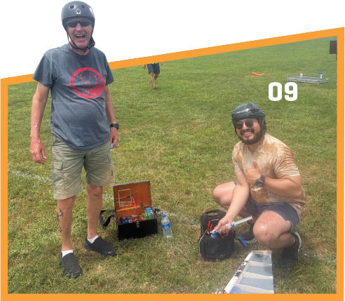 Two people outdoors wearing helmets, with toolboxes on grass, number 09 on image.