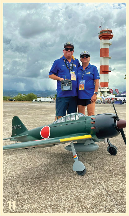 Two people in blue shirts stand with a model plane near a control tower.
