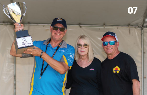 Three people posing with a large trophy, number 07 visible in the corner.