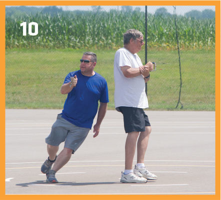 Two men playing bocce on a court, with a field in the background.