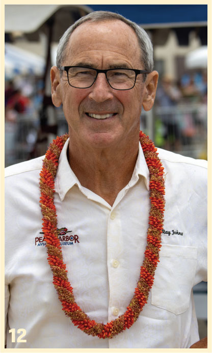 Man wearing a red lei, white shirt with "PEARL HARBOR AVIATION MUSEUM" text, smiling.
