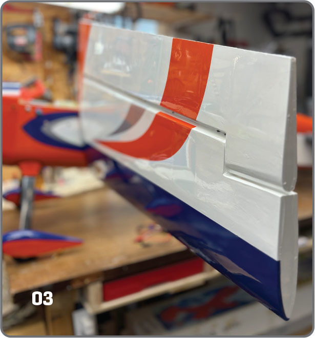 Model airplane tail with red, white, and blue stripes on a workbench.