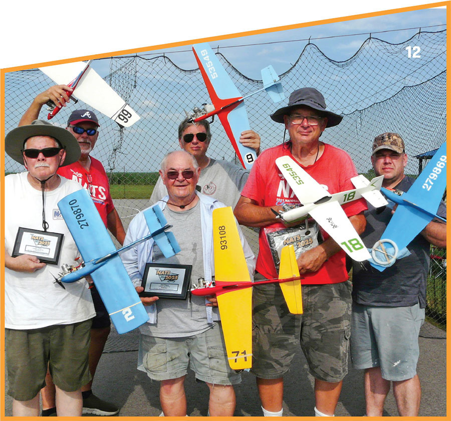 Group of men holding model aircraft and plaques, standing in front of a net fence.