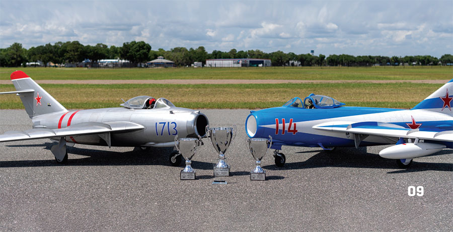 Two model jets with trophies, one silver labeled "1713," one blue labeled "114," on a runway.