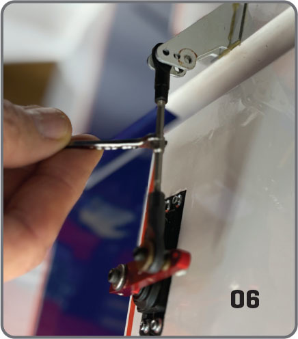 Hand adjusting a model airplane control linkage, number 06 shown.