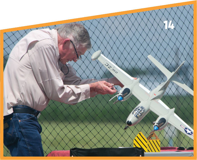 Man adjusting a model airplane near a chain-link fence.