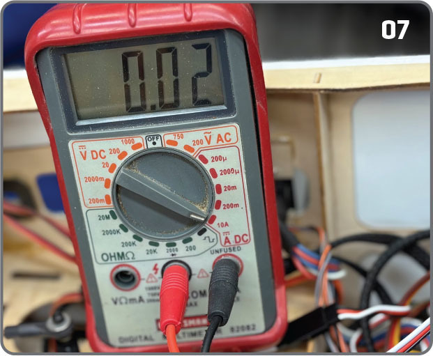 Red digital multimeter showing 0.02, wires attached.
