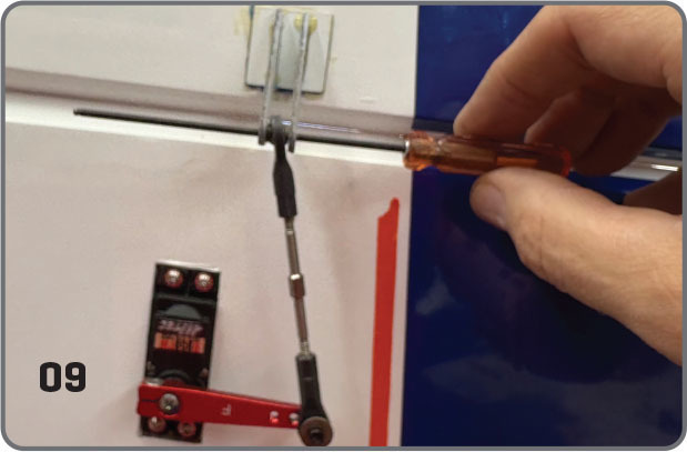 Hand adjusting airplane control pushrod with a screwdriver; number 09 visible.