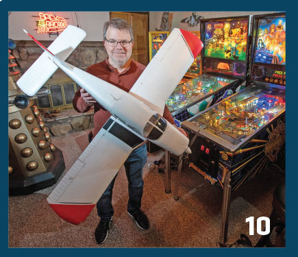 Man holding model airplane in game room with pinball machines. Number 10 in corner.
