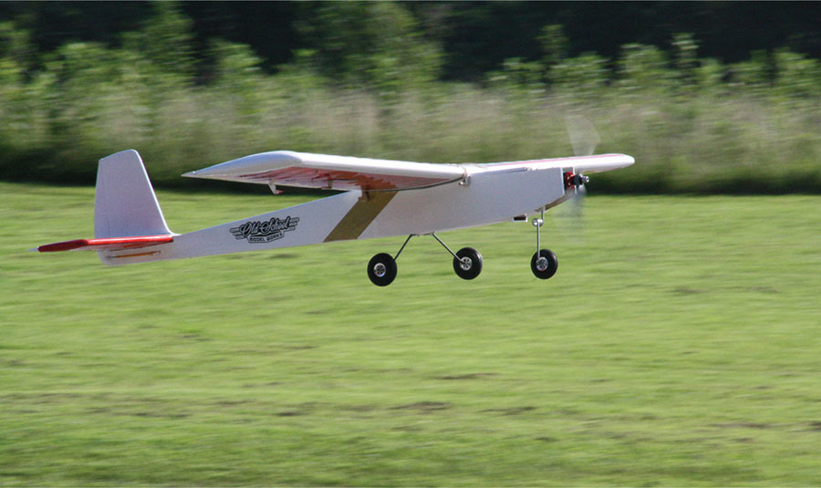 Remote control plane flying over a grassy field.