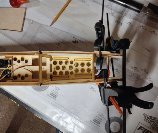 Model airplane fuselage under construction with clamps and drawing plans.