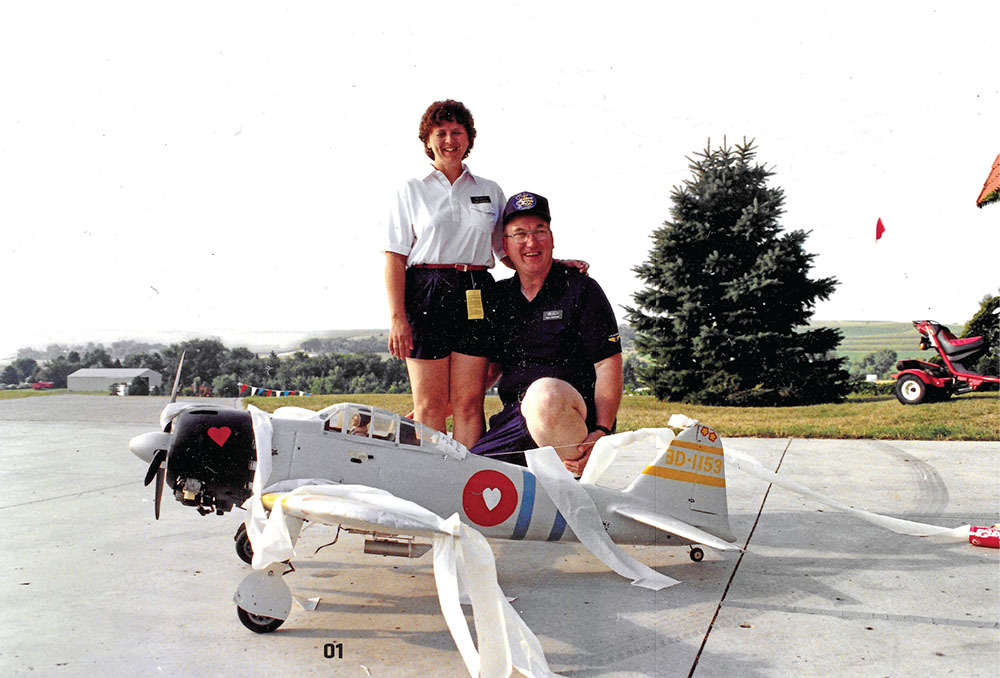 Couple smiling behind a small plane model on a sunny day.