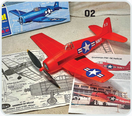 Red model plane on plans, box showing a blue version, labeled "Grumman F6F-5K Hellcat."