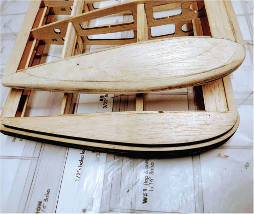 Wooden model airplane wing under construction on a plan sheet.